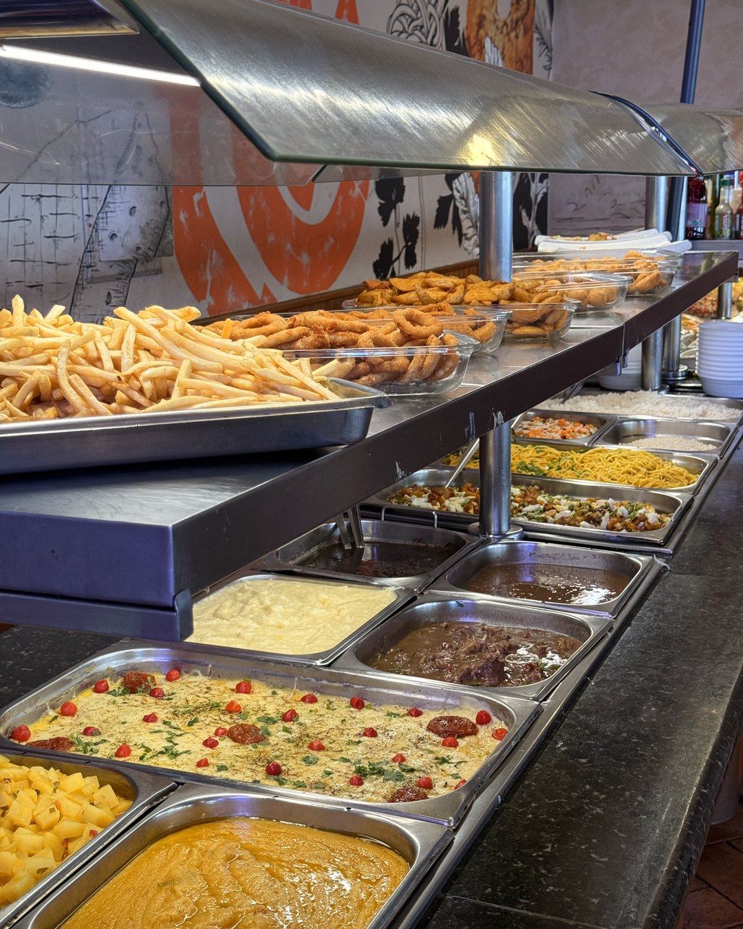 Buffet do self-service com batata frita, anéis de cebola, massas, purê e pratos quentes