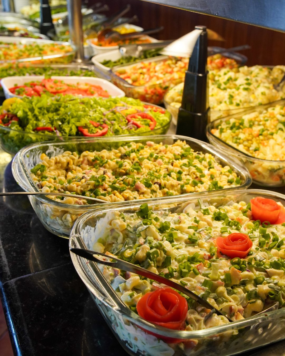 Bancada de saladas: macarrão, maionese, alface, tomate e legumes